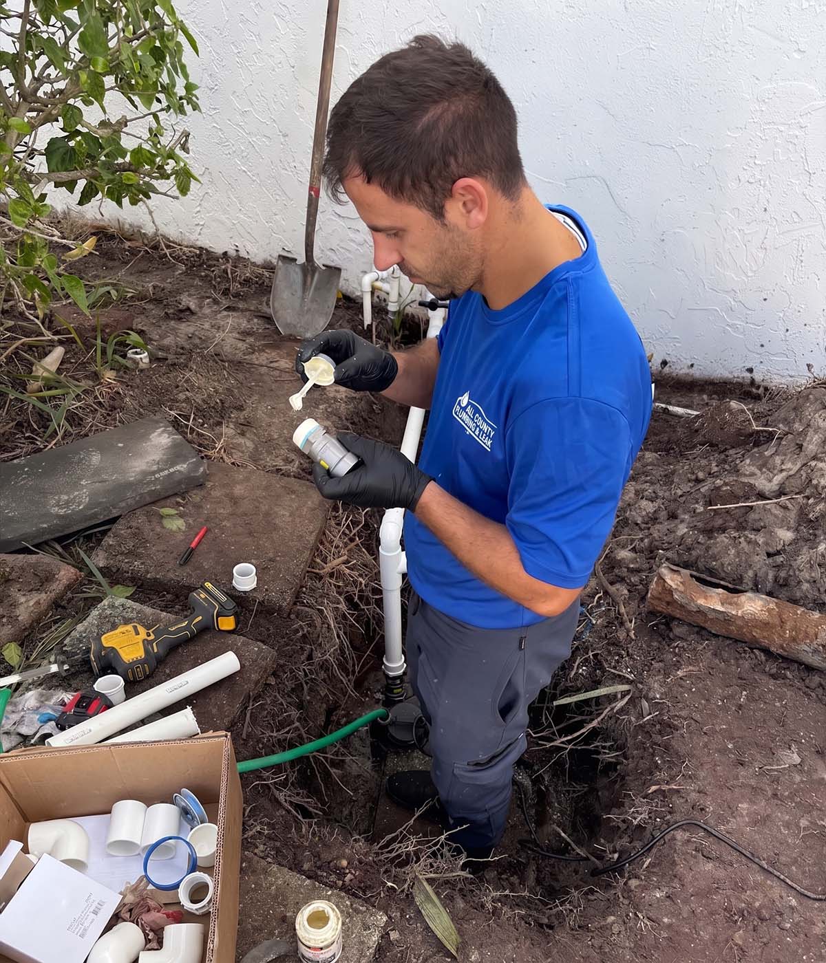 All County Plumbing & Leak technician applying primer to a PVC pipe fitting during an outdoor sewer line repair